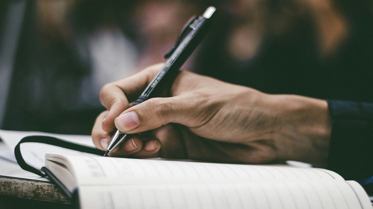 A close-up of a hand writing answers in a lined journal with a pen